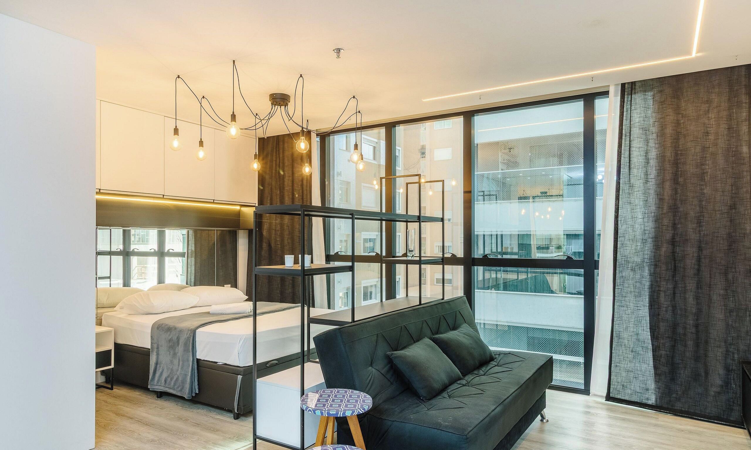 Een moderne hotelkamer met een bed, een bank, een kleine tafel en een groot raam met uitzicht op de stad.