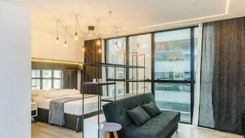 Een moderne hotelkamer met een bed, een bank, een kleine tafel en een groot raam met uitzicht op de stad.