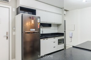 A modern kitchen with white cabinetry, a stainless steel refrigerator, a black countertop, and a built-in oven. - IFT - Ed. Infinity Tower Flat 350m From Meia Praia (Itapema)