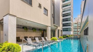 Une piscine avec des chaises longues et un bâtiment à plusieurs étages, doté de nombreuses fenêtres.