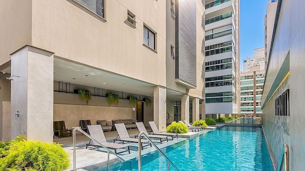 A swimming pool with lounge chairs and a building with multiple floors and windows. - IFT - Ed. Infinity Tower Flat 350m From Meia Praia (Itapema)