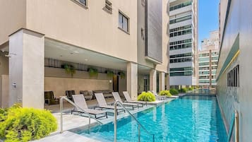 A swimming pool with lounge chairs and a building with multiple floors and windows.