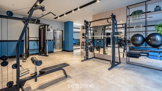 A modern gym with various exercise equipment, a mirrored wall, and a seating area. - IFT - Ed. Infinity Tower Flat 350m From Meia Praia (Itapema)