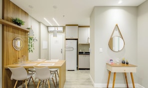 A modern kitchen with white cabinets, a refrigerator, and a dining area with a wooden table and chairs. - IFT - Ed. Infinity Tower Flat 350m From Meia Praia (Itapema)