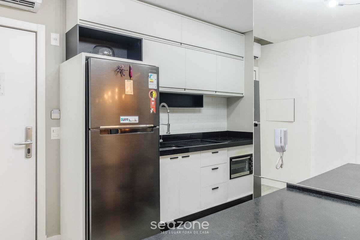A modern kitchen with white cabinetry, a stainless steel refrigerator, a black countertop, and a built-in oven.