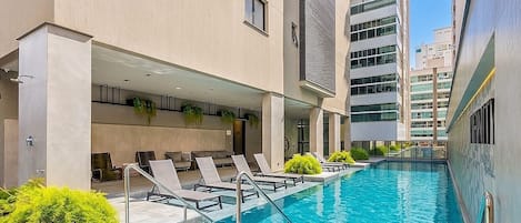A swimming pool with lounge chairs and a building with multiple floors and windows.