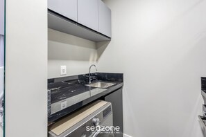 A compact kitchen with a black marble countertop, stainless steel sink, and a built-in dishwasher. - IFT - Ed. Infinity Tower Flat 350m From Meia Praia (Itapema)