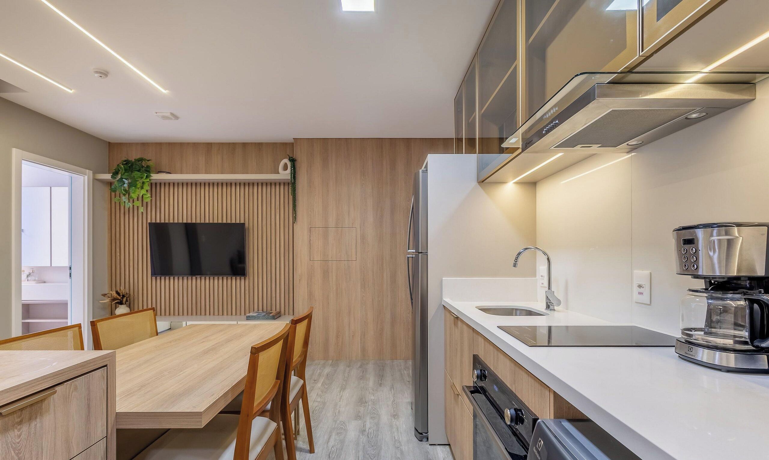 A modern kitchen with a built-in oven, a coffee machine, and a large flat-screen TV mounted on the wall.