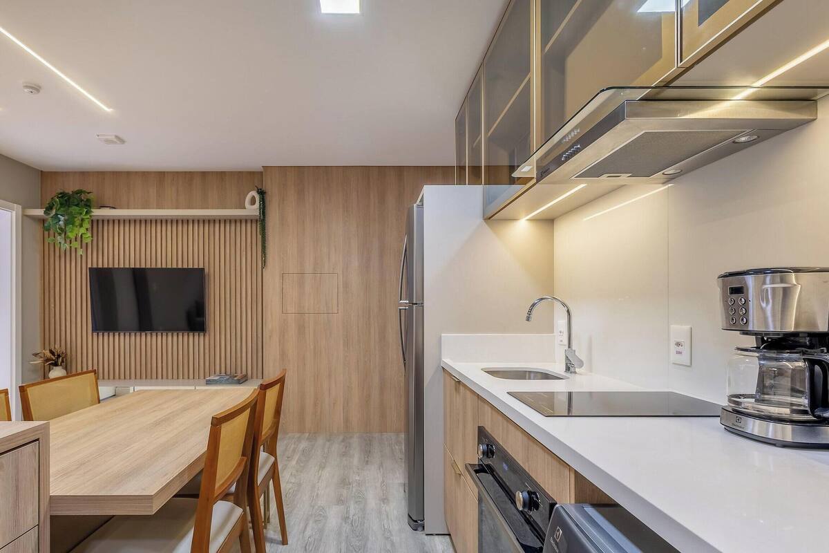 A modern kitchen with a built-in oven, a coffee machine, and a flat-screen TV mounted on the wall.