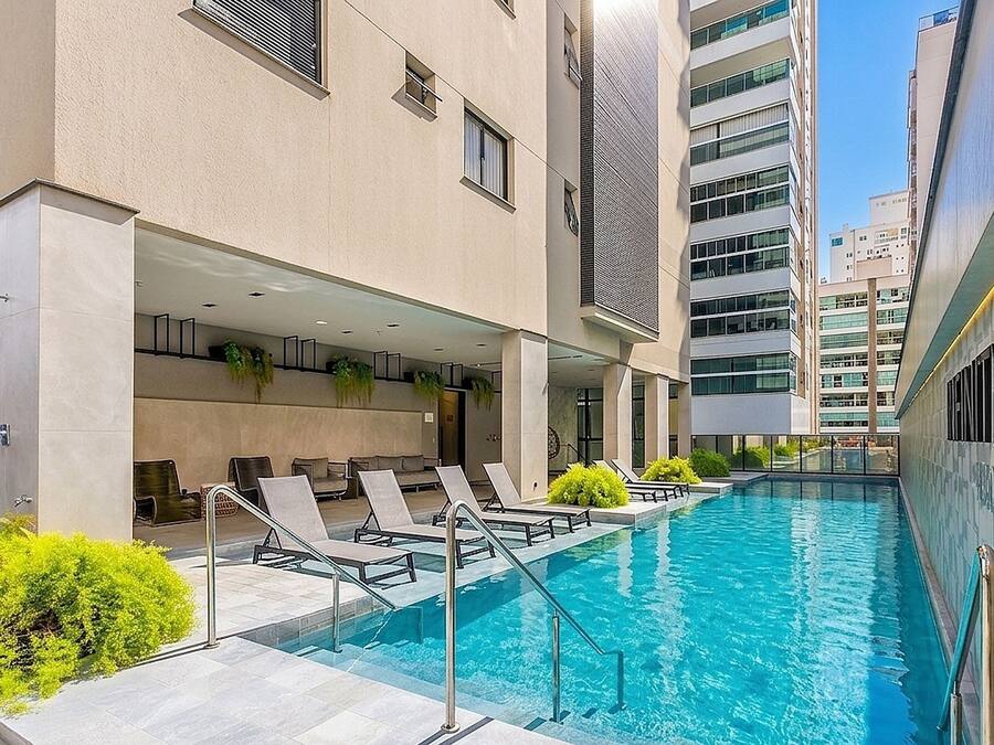A swimming pool with lounge chairs and a building with multiple floors and windows.