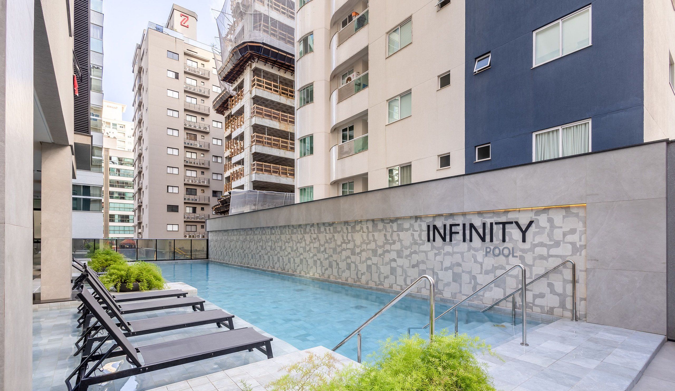 A modern building with a pool area, including lounge chairs and a staircase leading to the pool.