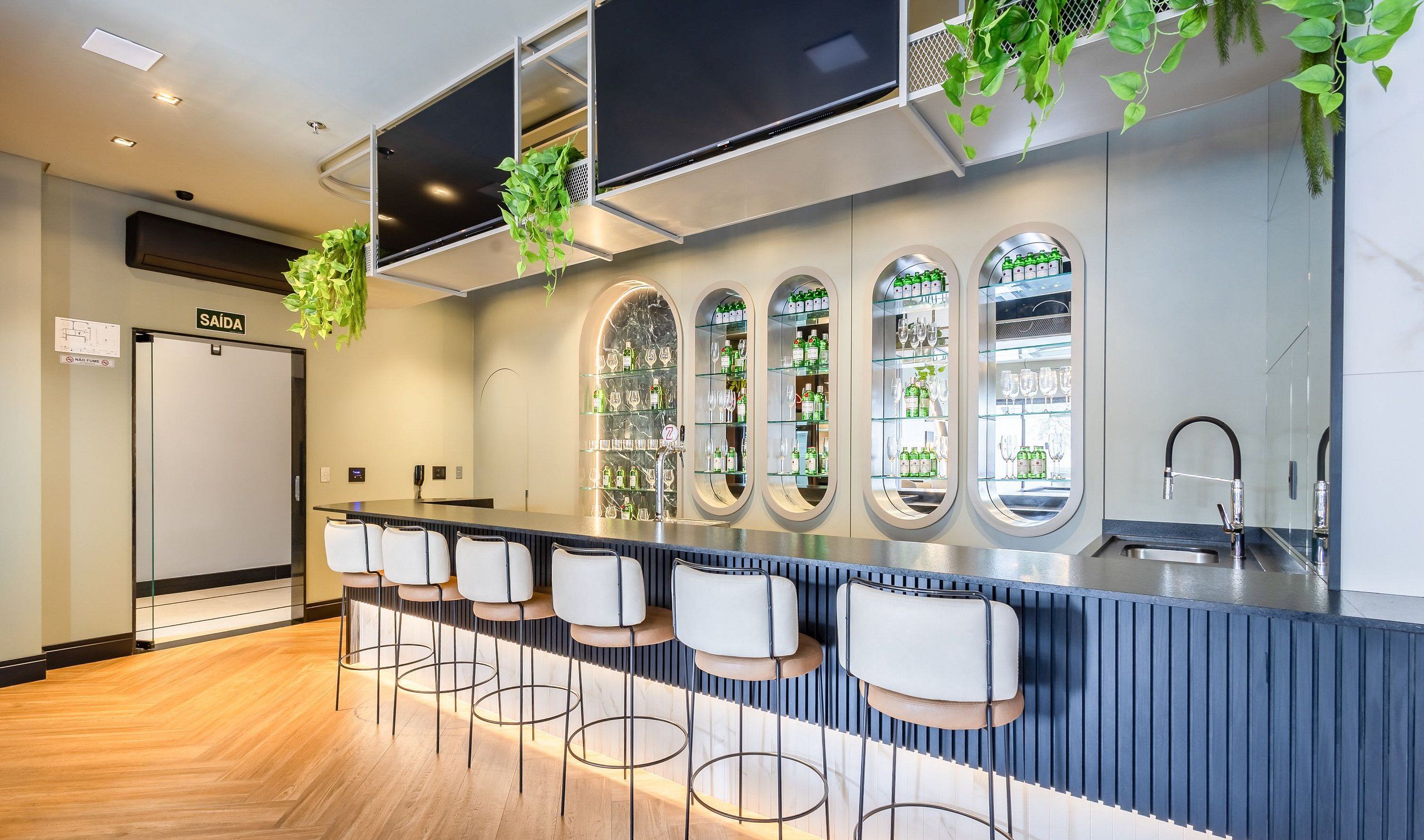 Uma área de bar moderna com um balcão extenso, vários bancos altos e uma grande tela de televisão.