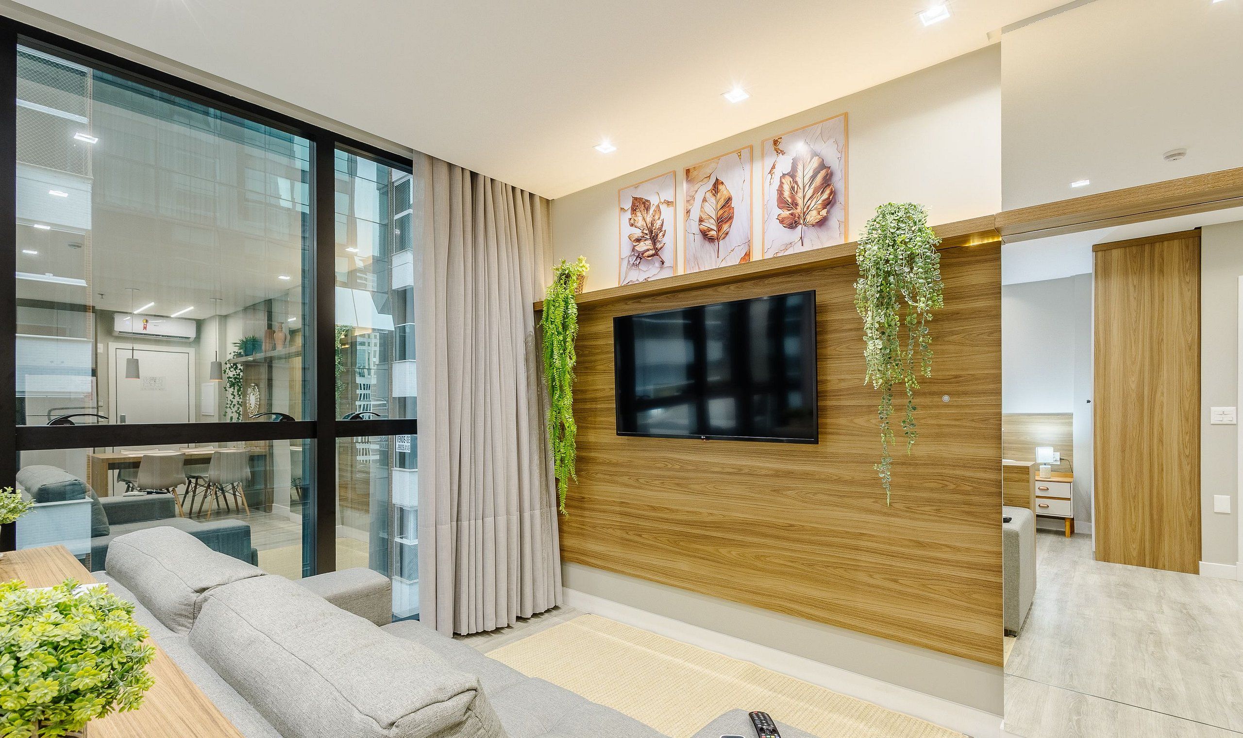 A modern living room with a large TV, wooden panel wall, and a glass partition.