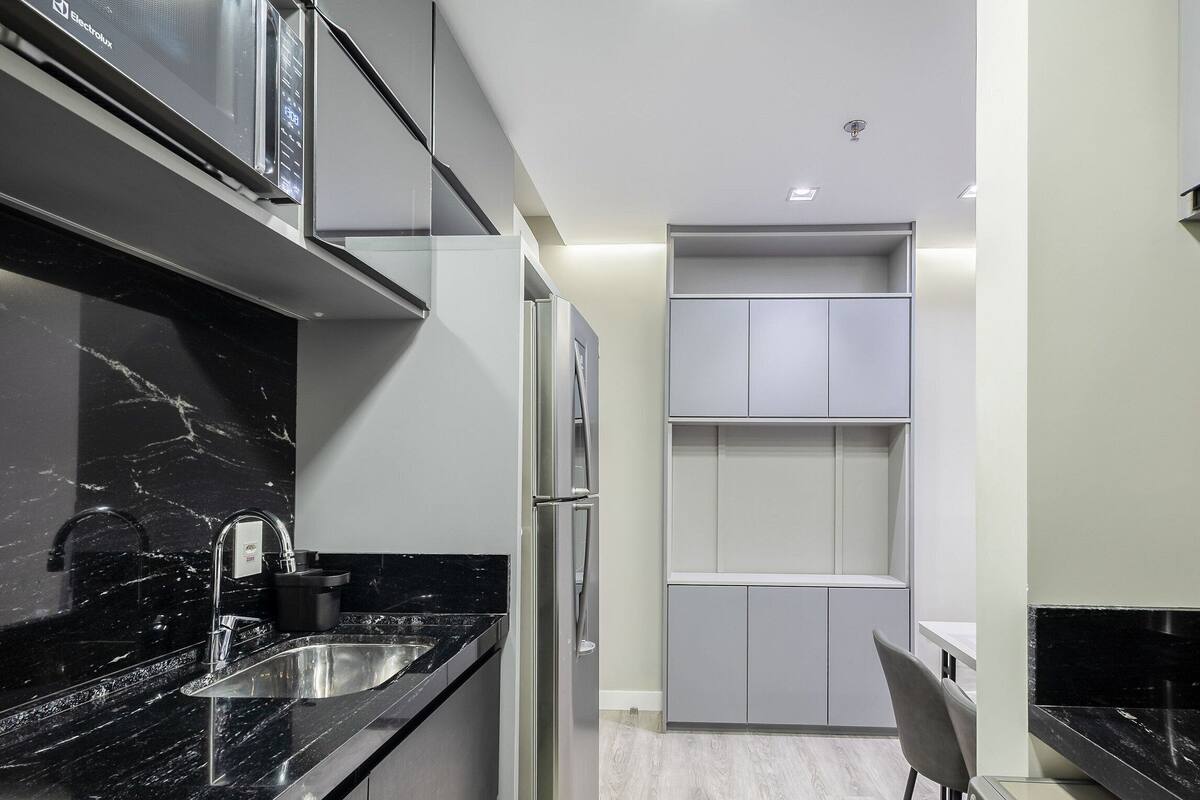 A modern kitchen with black marble countertops, stainless steel appliances, and grey cabinetry.