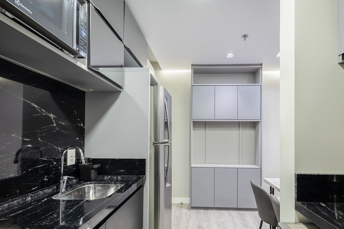 A modern kitchen with black marble countertops, stainless steel appliances, and grey cabinetry.