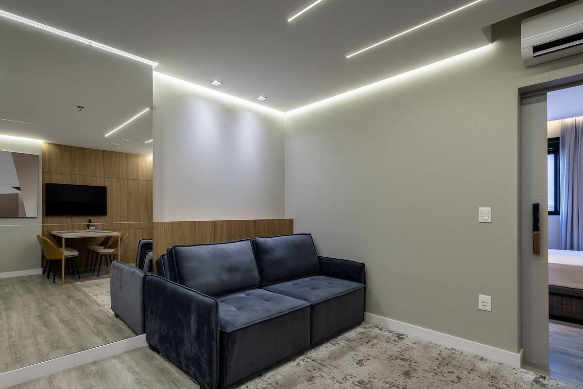 A modern hotel room with a sofa, a small desk, and a TV mounted on the wall.