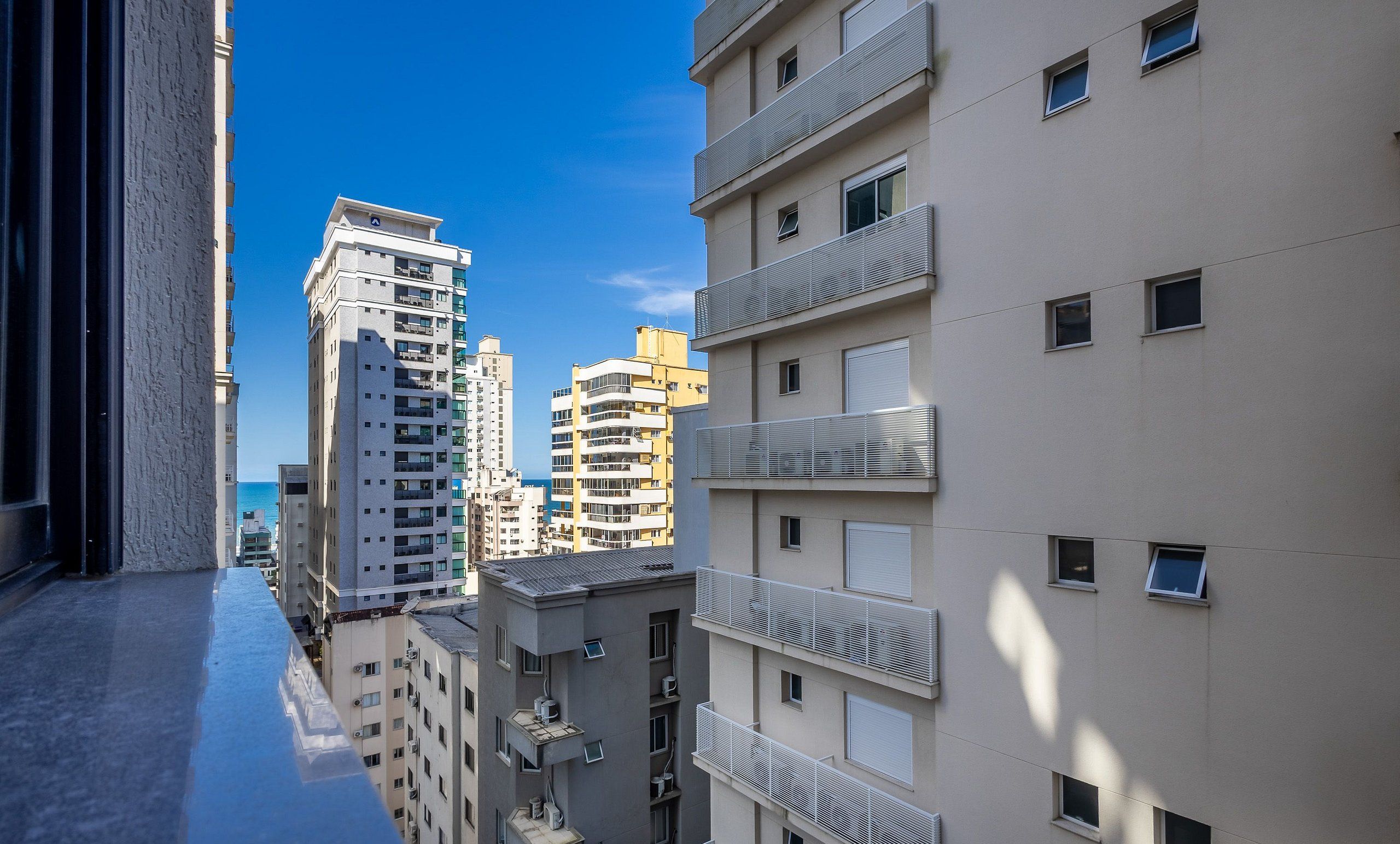 A high-rise residential building with multiple balconies and a clear view of the sea in the background.