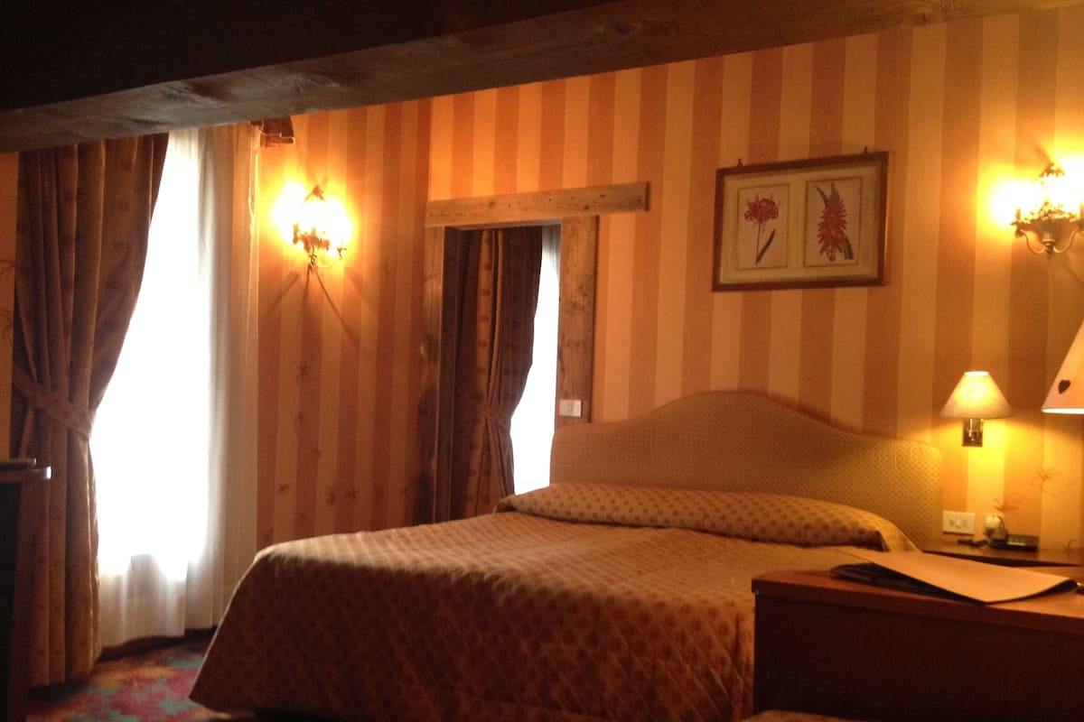 Una habitación de hotel con dos camas, papel tapiz a rayas, un cuadro en la pared y una mesita de noche con una lámpara.