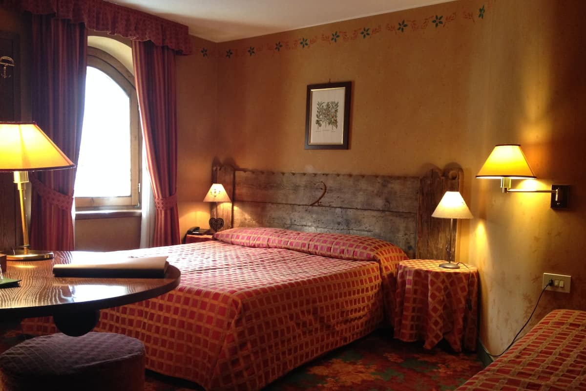 Una habitación de hotel con dos camas, un escritorio, una silla y un ventanal con cortinas.