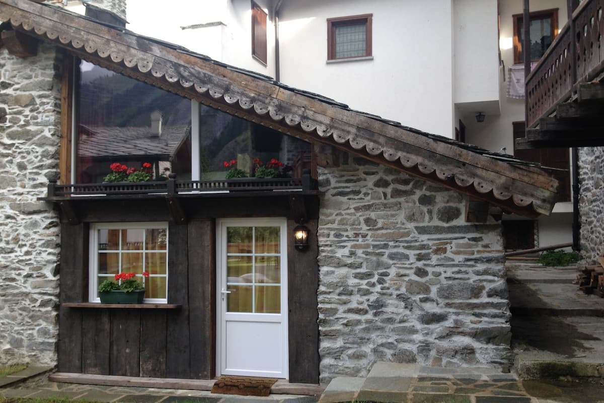 Un edificio de piedra con puerta y ventanas de madera, un balcón con flores y una escalera de piedra.