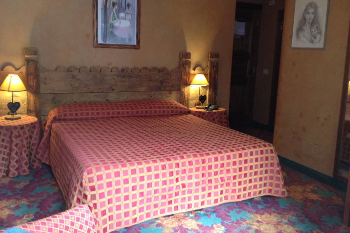 Habitación de hotel con una cama grande, dos mesitas de noche con lámparas, un cabecero y dos cuadros en las paredes.