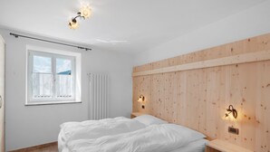 A bedroom with a bed, a window, a radiator, and wooden paneling on the wall. - Apartment 'Vich' with Mountain View, Balcony and Wi-Fi (Vigo di Fassa)