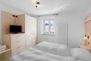Un dormitorio con cama, armario de madera, televisor, ventana y radiador.