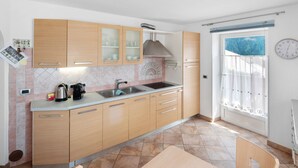 A kitchen with wooden cabinets, a sink, and a window with a curtain. - Apartment 'Vich' with Mountain View, Balcony and Wi-Fi (Vigo di Fassa)