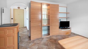 A room with a curved wooden cabinet, a television on a stand, and a bench. - Apartment 'Vich' with Mountain View, Balcony and Wi-Fi (Vigo di Fassa)