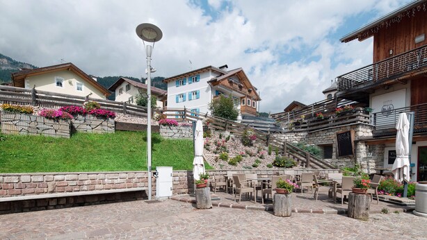 A courtyard with outdoor seating, stone walls, and a staircase leading to a building with a balcony. - Apartment 'Vich' with Mountain View, Balcony and Wi-Fi (Vigo di Fassa)