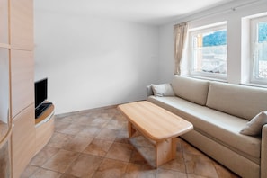 Habitación con sofá, banco de madera, televisión y ventana con vista a un edificio y árboles.