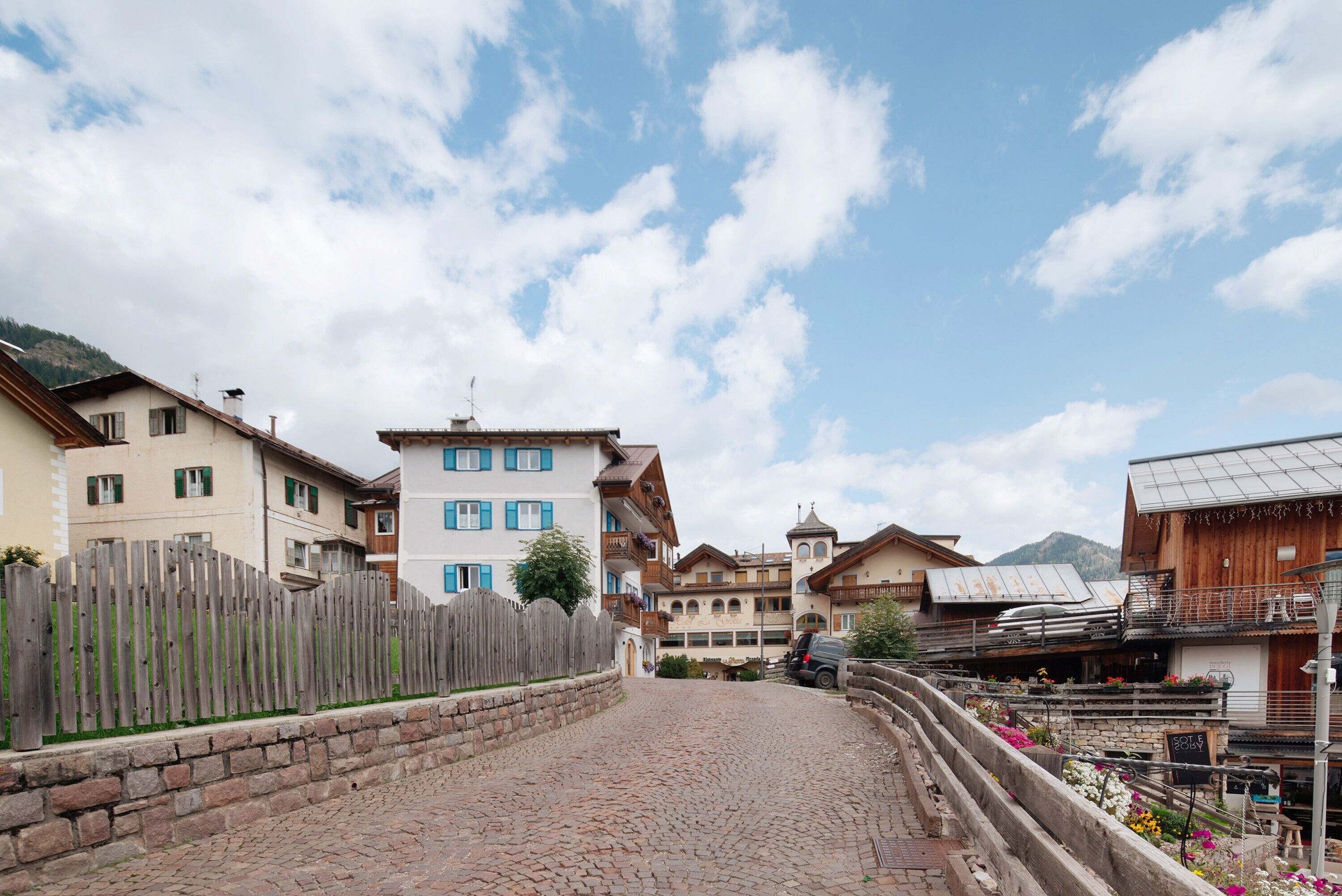 A cobblestone street lined with traditional buildings, a wooden fence, and a mountain in the background.