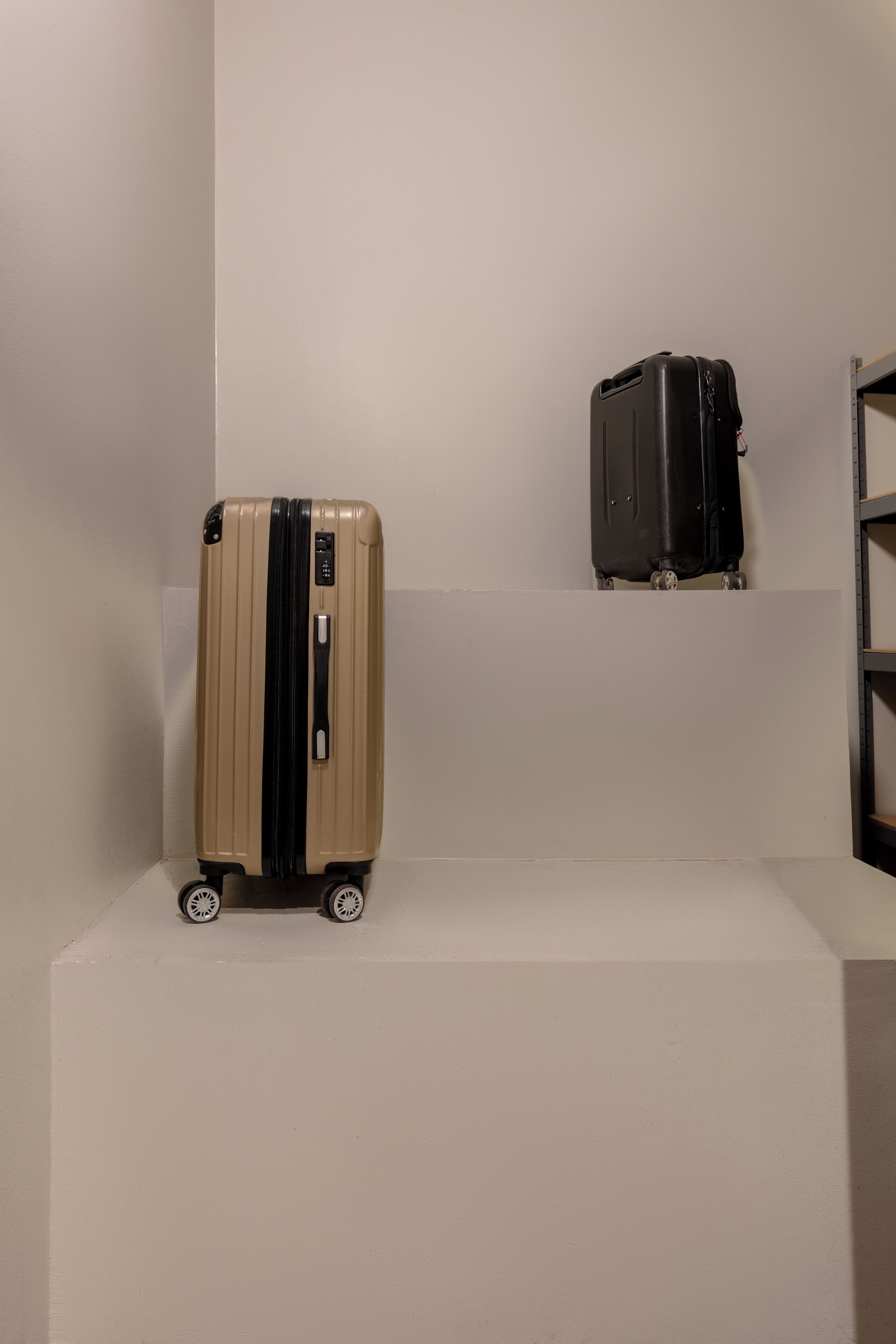 A beige suitcase with wheels and a black handle on a white platform.