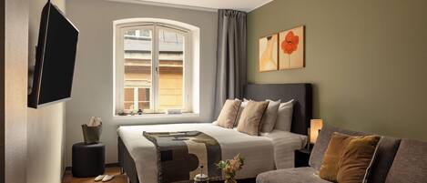 A hotel room with a bed, a sofa, a TV, a window with curtains, a bedside table, and a nightstand.