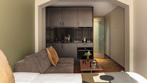 Un espacio habitable compacto con kitchenette, un sofá, una mesita de centro y una puerta que da a otra habitación.