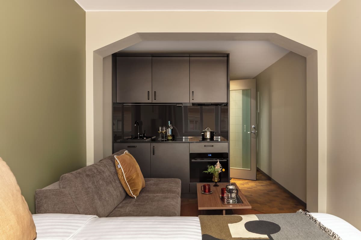 Un espace de vie compact comprenant un coin cuisine, un canapé, une table basse et une porte donnant sur une autre pièce.