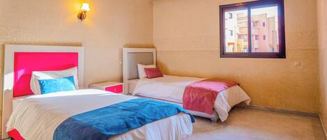 A hotel room with two beds, a nightstand, a wall-mounted TV, and a window with a view of buildings.