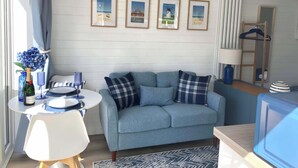 Ein modernes Wohnzimmer mit einem hellblauen Sofa, einem runden weißen Tisch mit einer Champagnerflasche und gerahmten Bildern an der Wand.