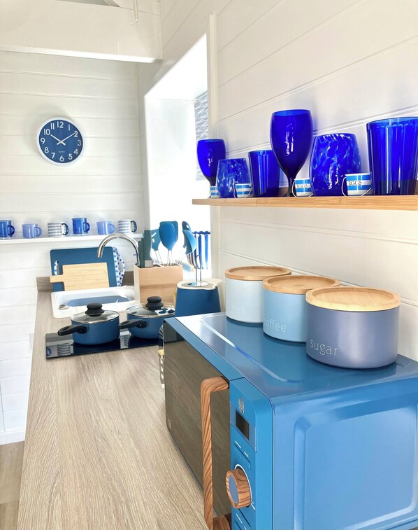 Una cocina moderna con electrodomésticos azules, un reloj y vajilla azul en estantes.