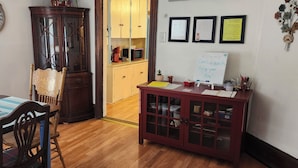 A dining area with a wooden table and chairs, a cabinet with glass doors, and a whiteboard with a welcome message. - Watkins Glen Overlook Apt (Watkins Glen)
