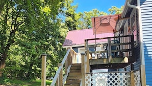 A wooden staircase leading to a deck with a red roof, surrounded by a lattice fence and two trash bins. - Watkins Glen Overlook Apt (Watkins Glen)
