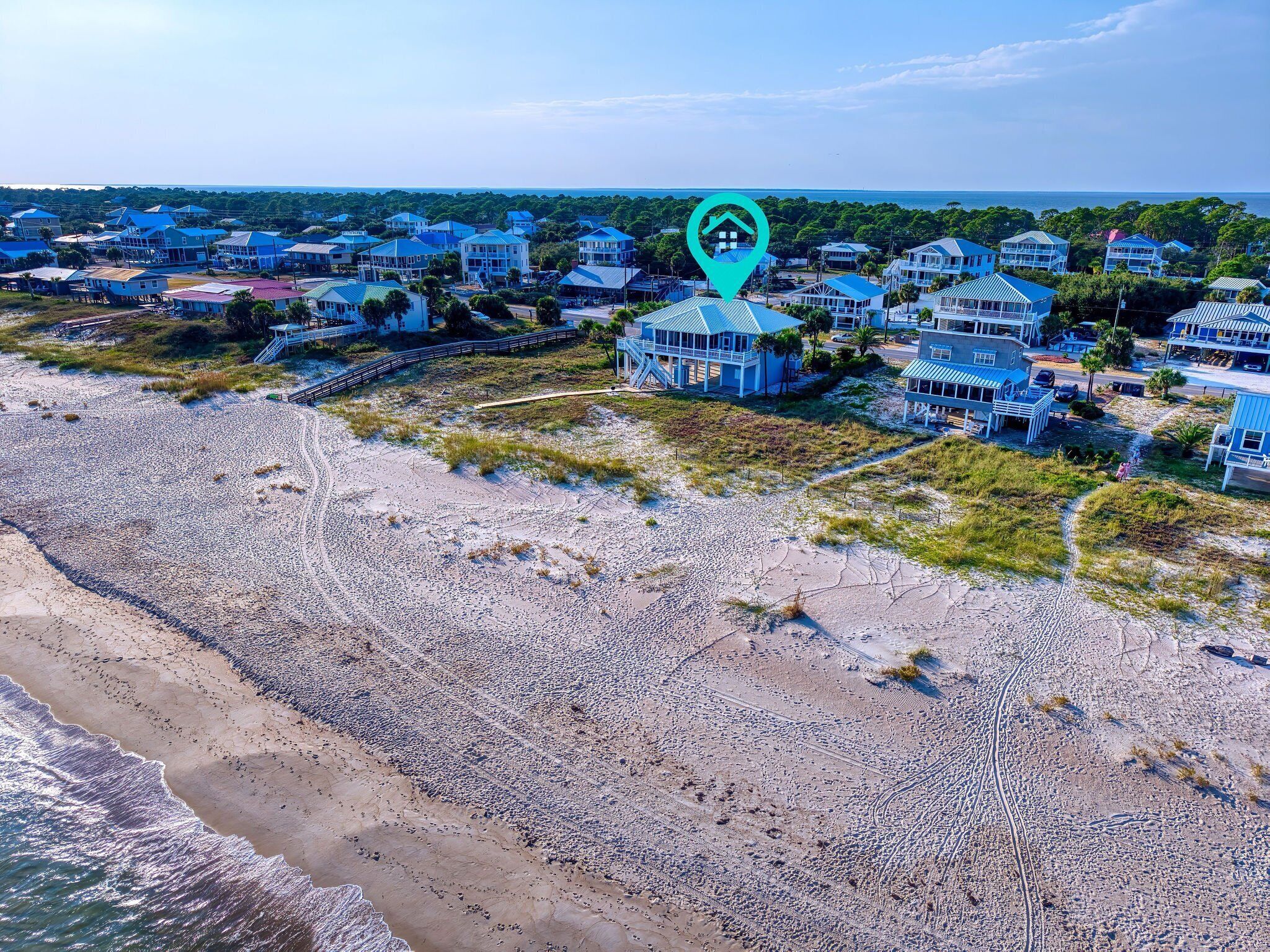 An aerial view of a coastal residential area with beachfront properties, a boardwalk, and a clear view of the ocean.