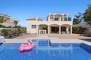Une maison moderne à deux étages avec une piscine, du mobilier d’extérieur et un flotteur en forme de flamant rose.