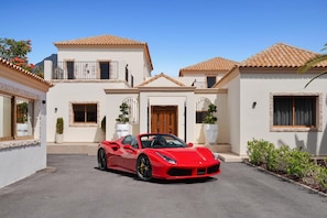 Une voiture de sport rouge est garée devant une maison dont le toit est recouvert de tuiles et qui possède une porte en bois.