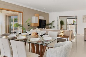 Un coin repas avec une table en verre, des chaises blanches et un canapé en arrière-plan.