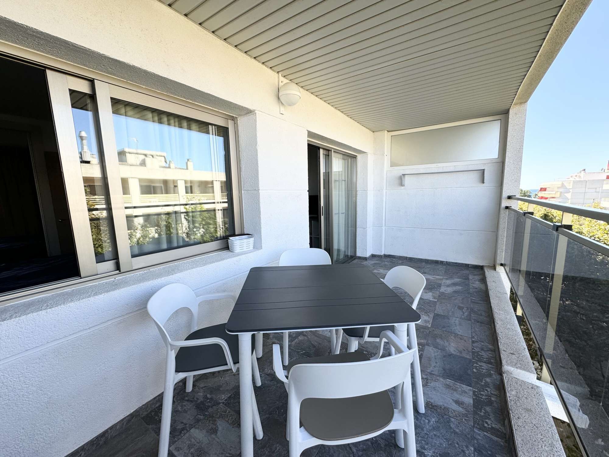 Een balkon met een tafel, stoelen, een schuifpui en uitzicht op gebouwen.