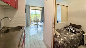 Una habitación pequeña con cama, ventana, lavamanos y balcón con sillas.