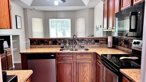 Une cuisine dotée de plans de travail en granit, d’armoires en bois, d’un lave-vaisselle, d’une cuisinière et d’un four à micro-ondes.