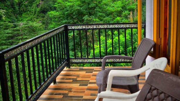 Una terraza de madera con barandilla, dos sillas y vistas a un bosque frondoso.