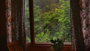 Una habitación con una cama, un ventanal con cortinas y vista a un bosque.